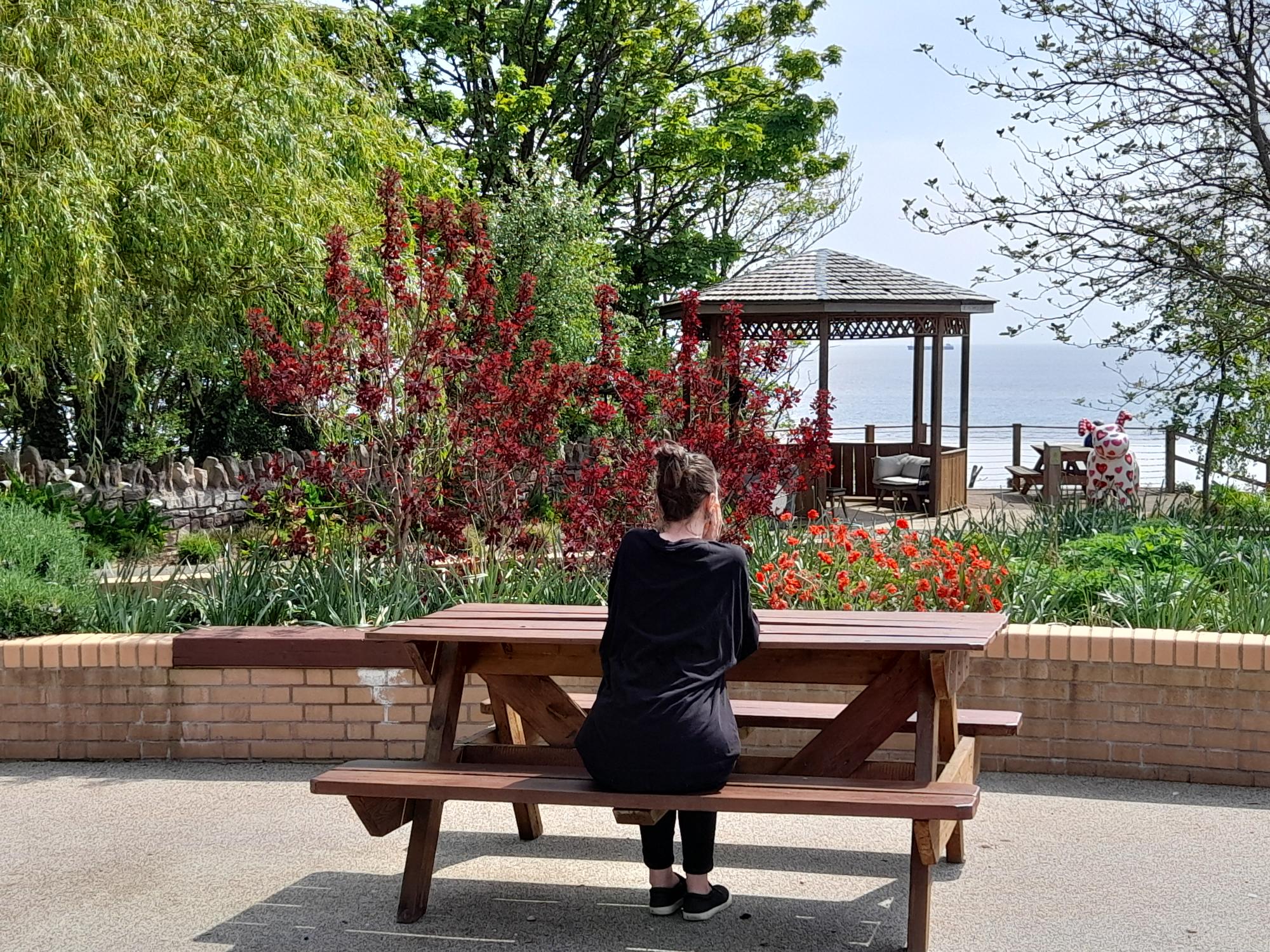 Solitary woman looks pensively out to sea while sitting in Ty Hafan's memorial garden