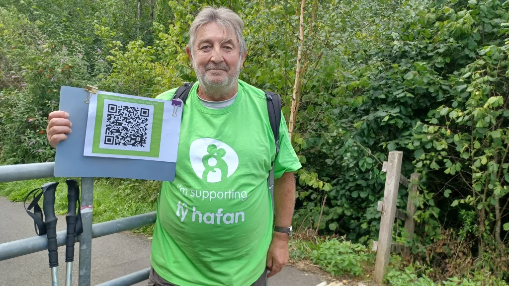 Huw Davies on a training walk holds up a QR code 