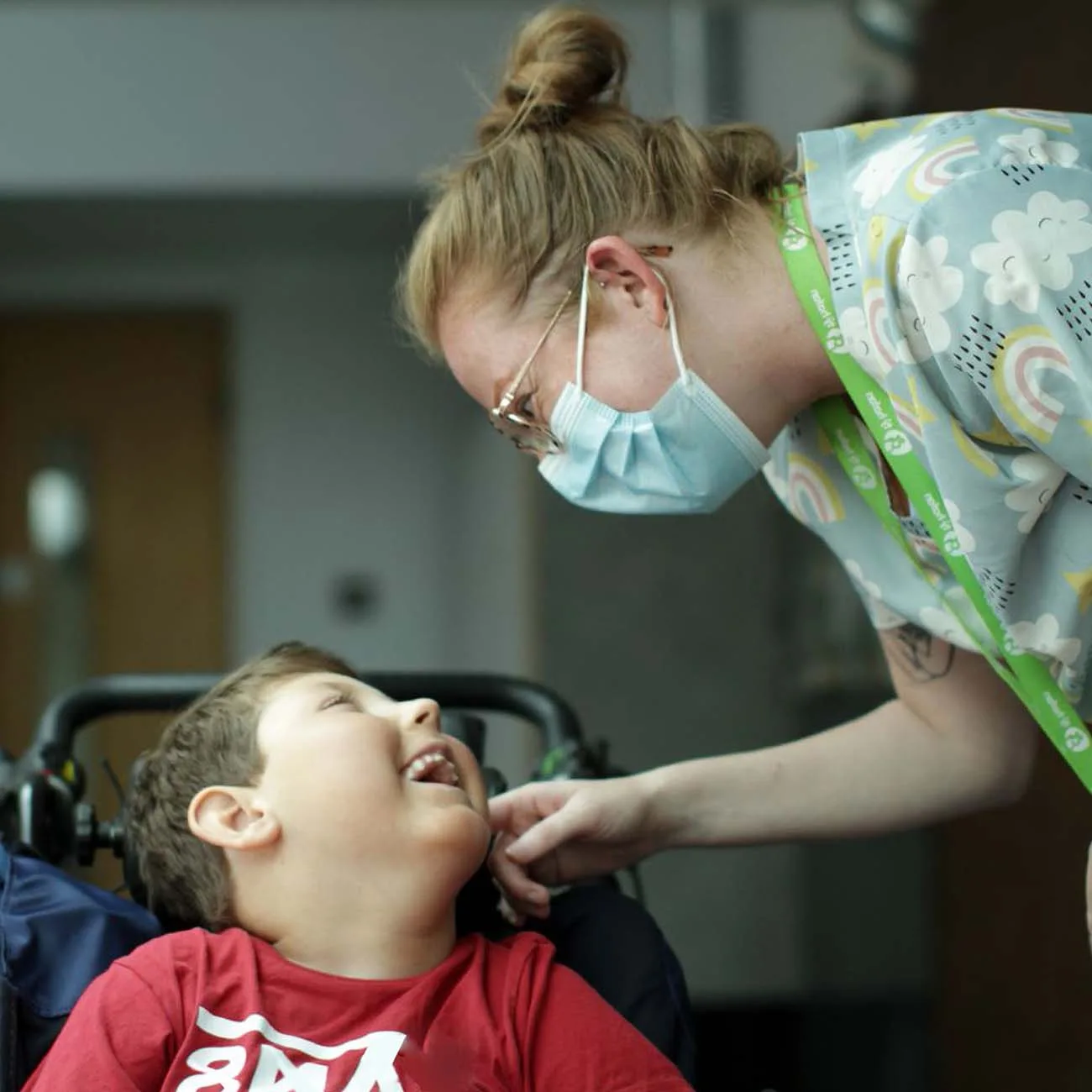 A photo of a nurse wearing a mask, reaching towards a child who is smiling