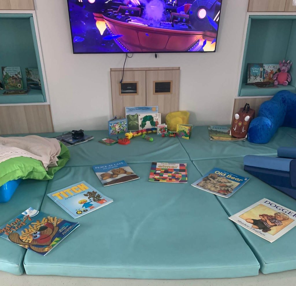 A photo of several books laid out on soft mats at the hospice, in front of the TV.