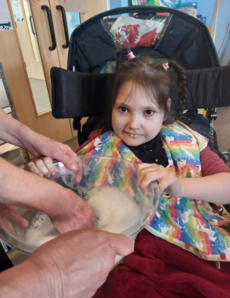 A photo of a young girl, Mared, who is playing with a bowl of soapy water. Mared's garden was cleared by our Family Support Volunteer gardeners