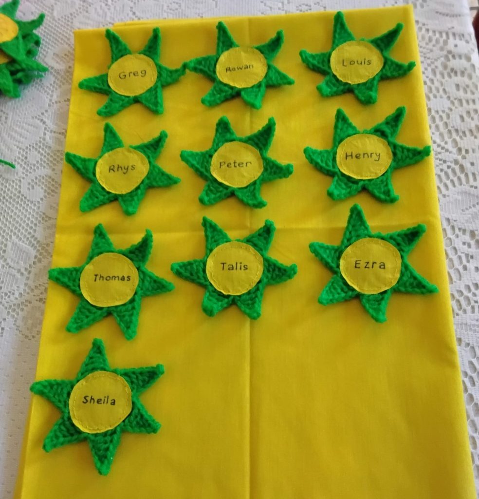 A yellow cape with green knitted stars on it with names on each star