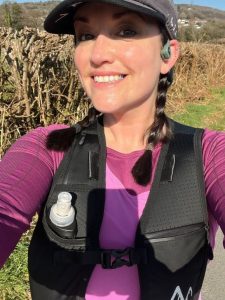 A selfie of Rhiannon, wearing a purple shirt, black running vest and black cap