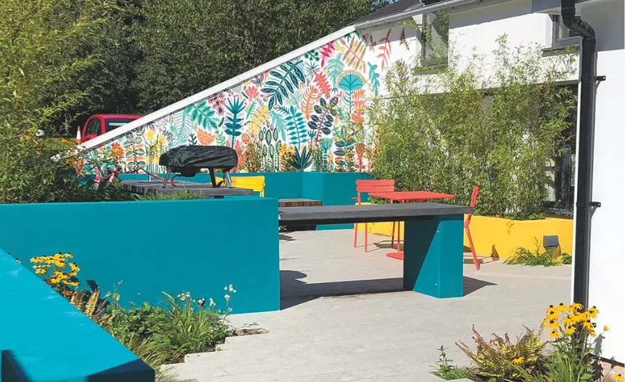 Outdoor space at The Den. There is a floral mural, red and yellow tables and chairs and a pizza oven