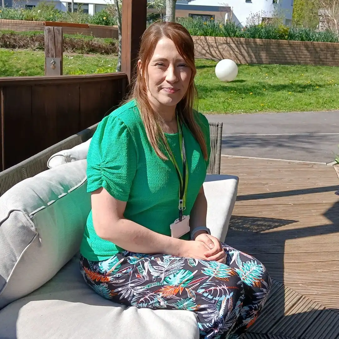 A photo of Jemma sat outside on a comfy bench in the sun. Jemma is a Neonatal Palliative Care Clinical Nurse Specialist