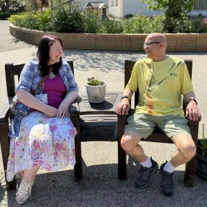 Johnny and Michele sit on a bench at the hospice, looking at each other and smiling
