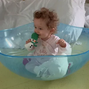 Willow-Rae sits in a wobble bowl, chewing on a knitted snowman