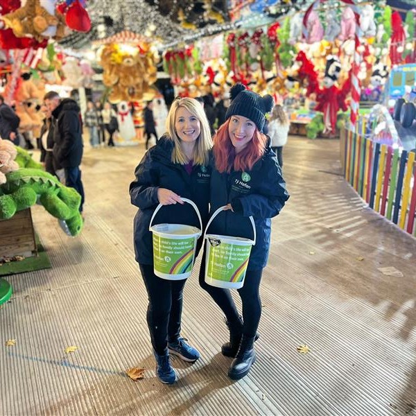A photo of two fundraisers smiling at the camera, holding Tŷ Hafan donation buckets at the Cardiff Winter Wonderland